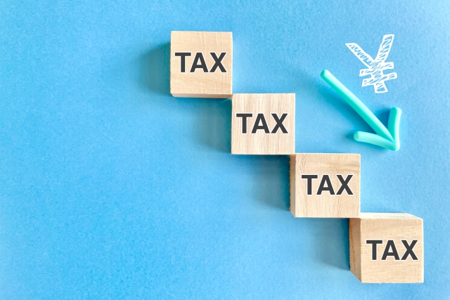 TAXの文字列が書かれた積み木と下向きの矢印、税金が下がるイメージ